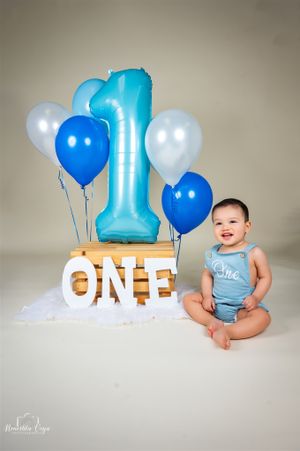 First birthday photo shoot with blue and white balloons and a large number one decoration.