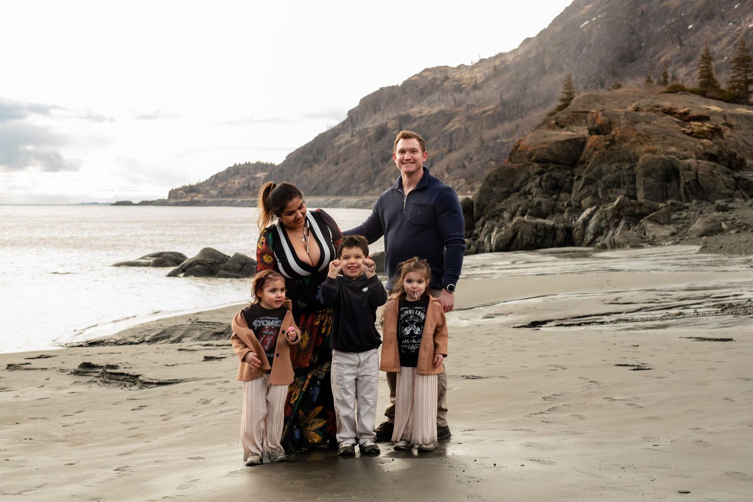 A family stands together on a scenic beach with cliffs and ocean waves in the background.