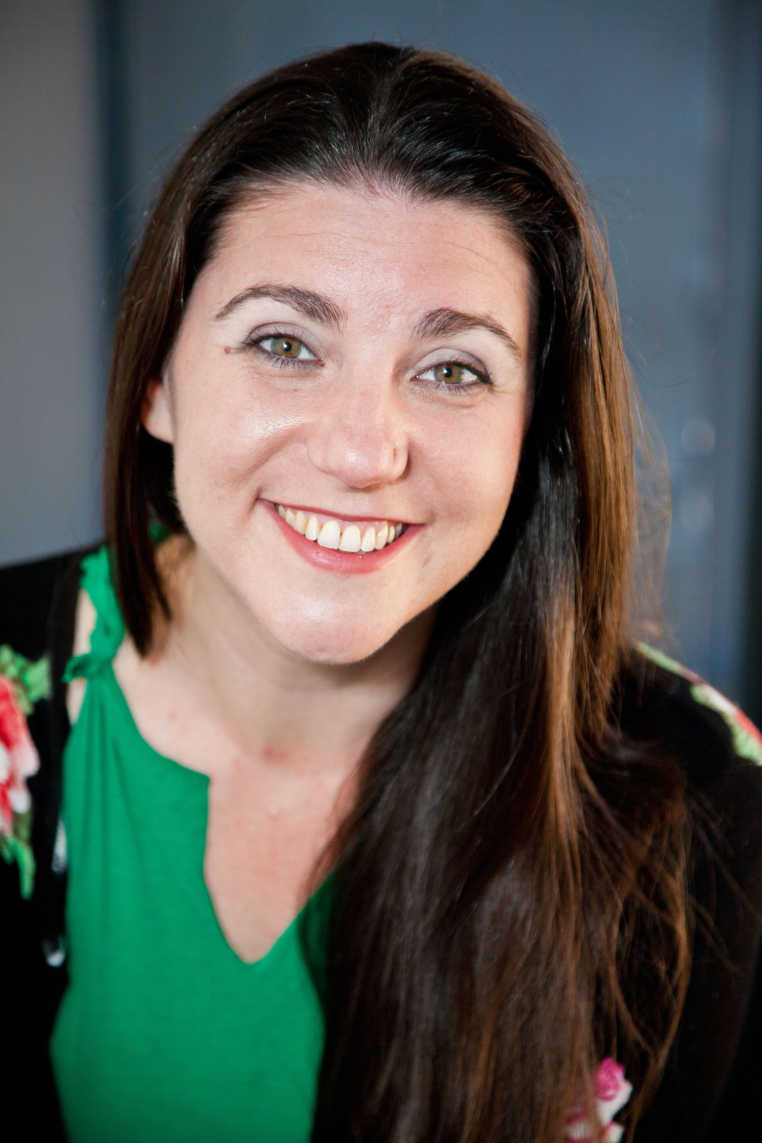 Portrait of person in green floral top with long dark hair against dark background.