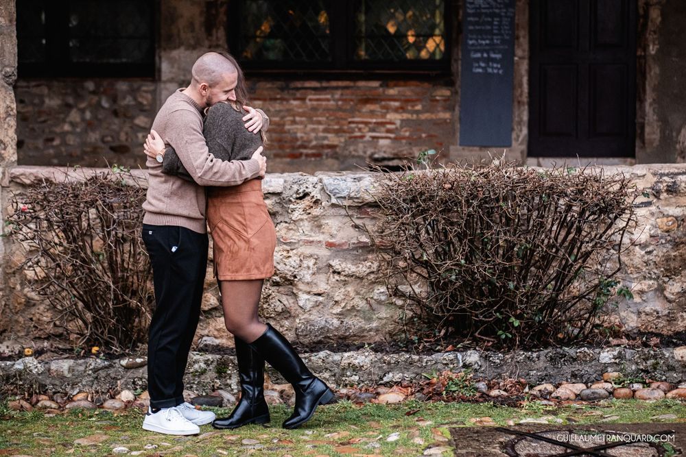 Couple sharing tender moment outdoors near historic stone building and garden.