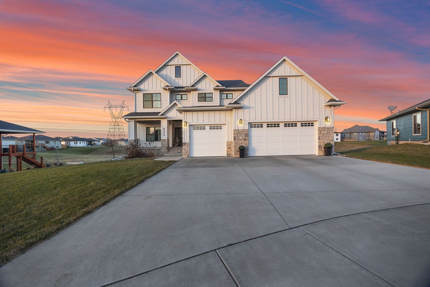 Modern farmhouse style home with three car garage at sunset featuring dramatic orange and purple sky.