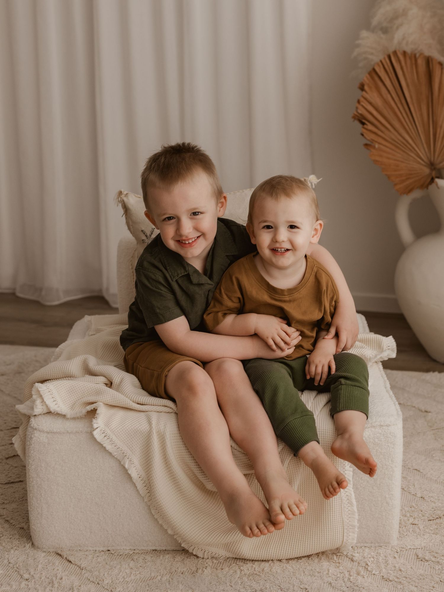 Two young siblings share joyful moments while sitting together on a white cushion.