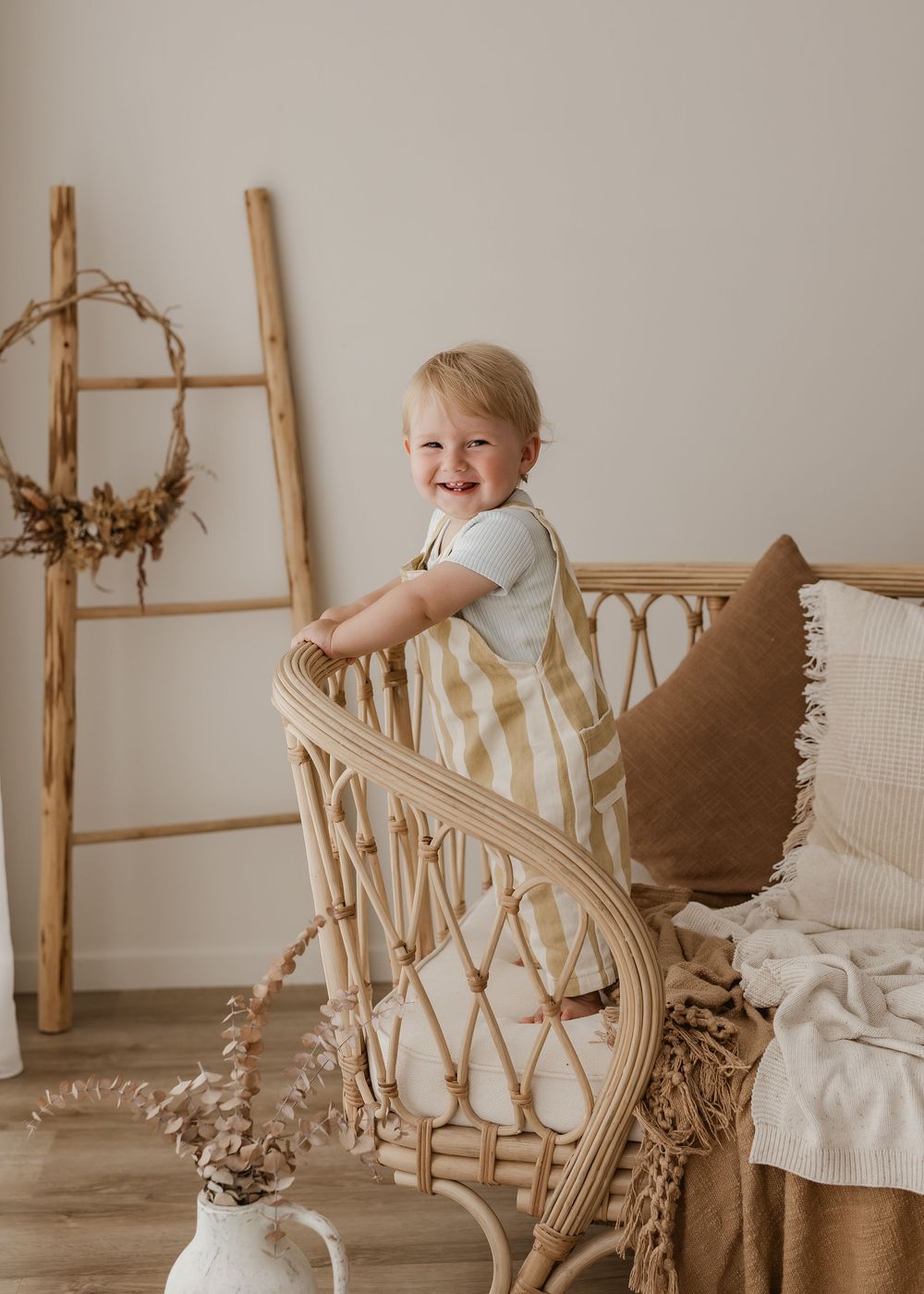 A child plays on a vintage rattan chair in a cozy neutral-toned room with natural decor elements.