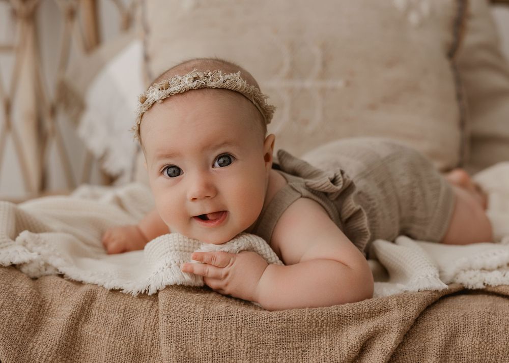 Five neutral-toned photographs showing a baby lying on beige linen bedding in different poses.