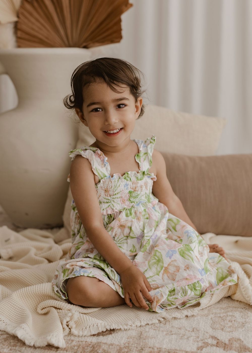 A small child wearing a floral dress lies on a beige couch in a series of playful poses.