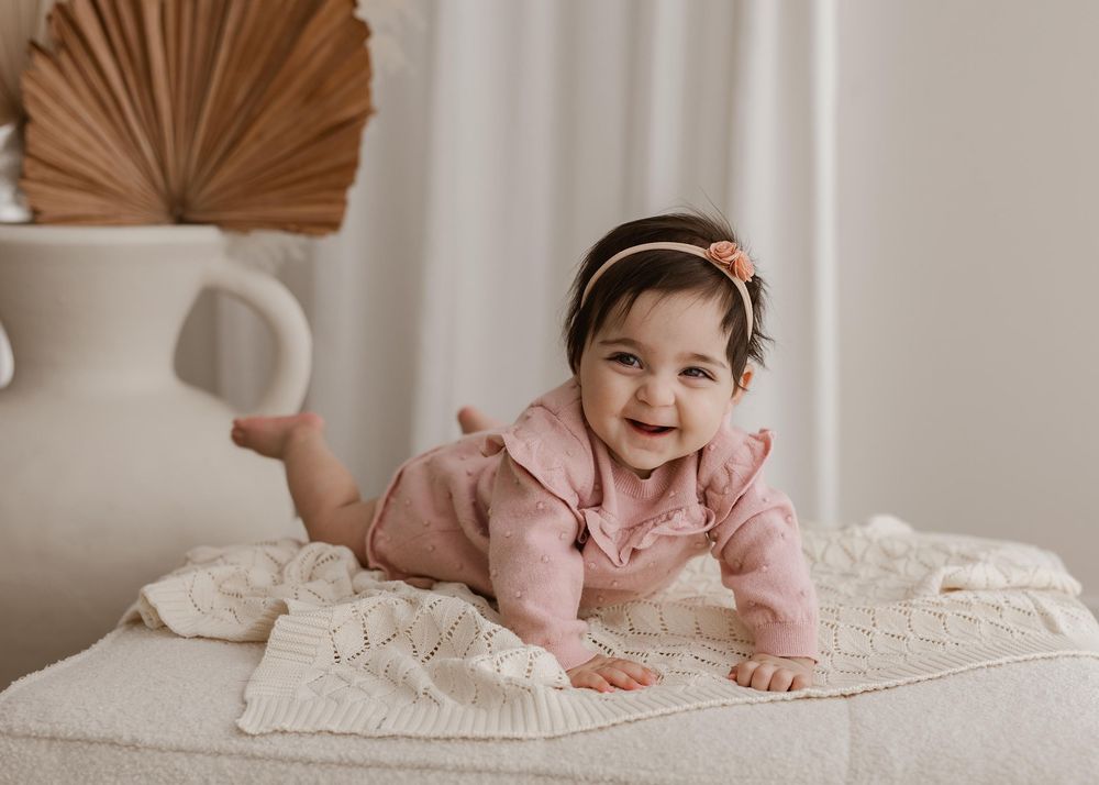 A sequence of photos showing a baby rolling and playing on a white blanket in a neutral-toned room.
