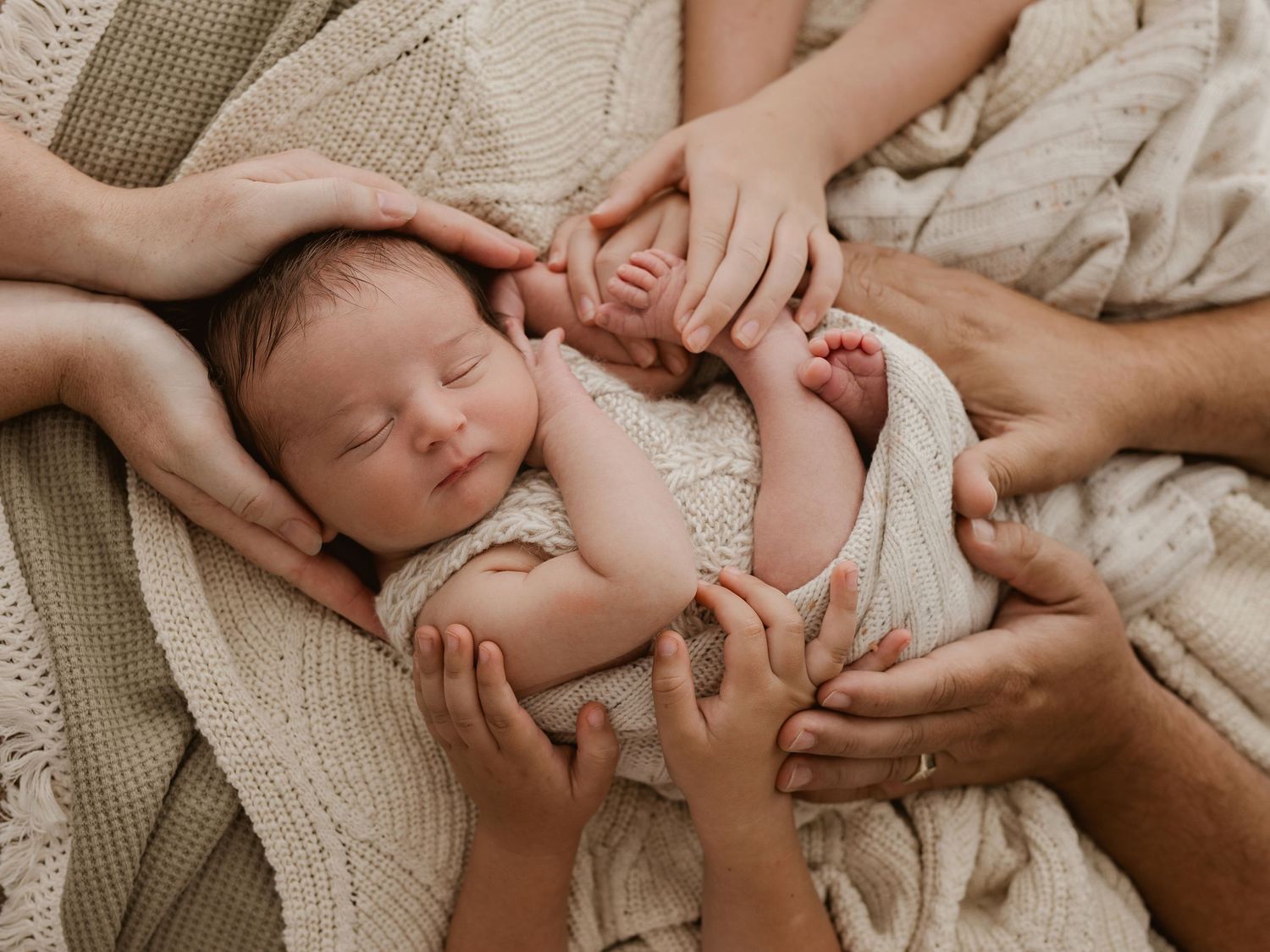 Peaceful sleeping newborn wrapped in soft white blanket against neutral background.