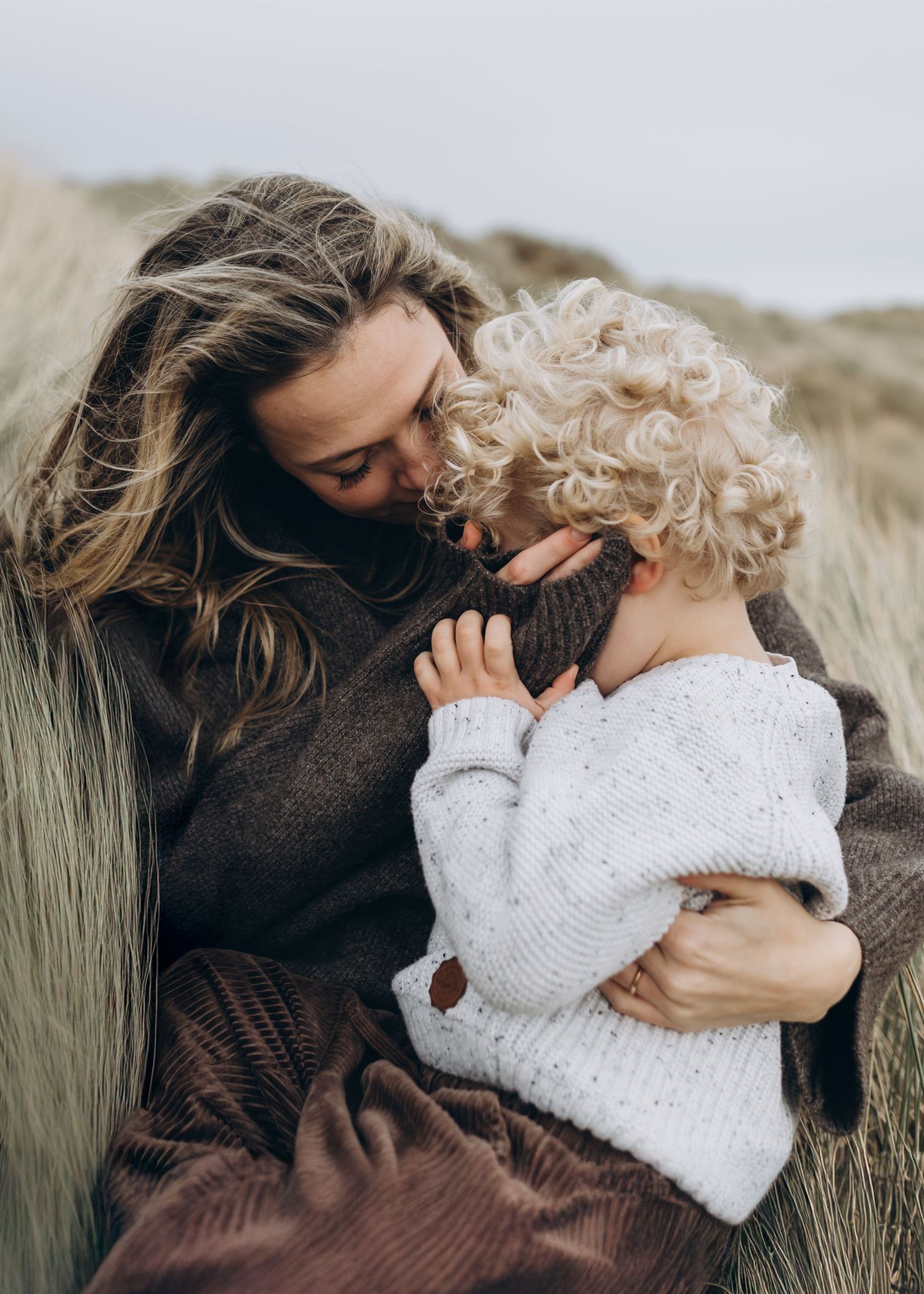A mother kissing her son's head during their photo session with Forever Ours Photography in Camber Sands, Kent, UK
