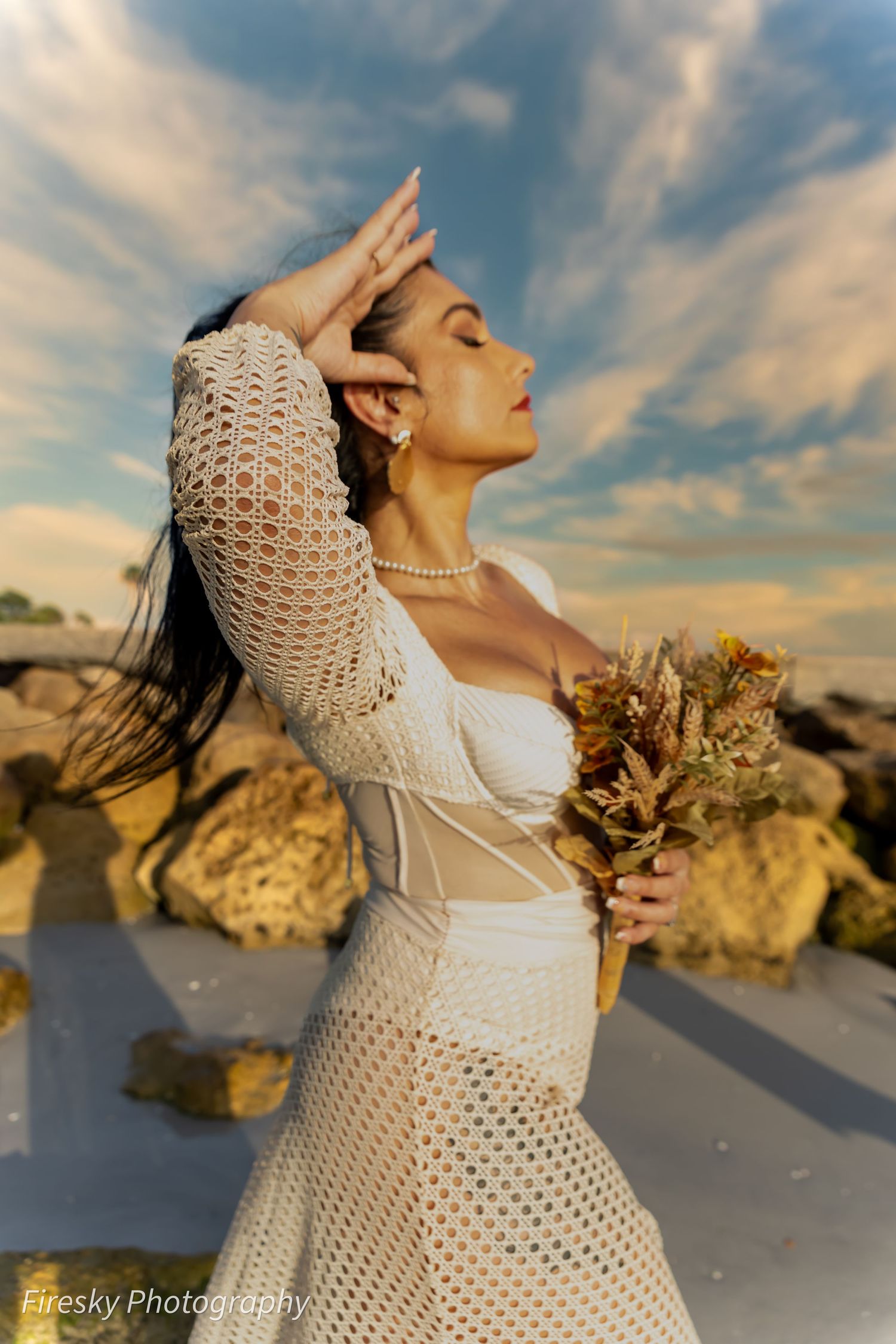 Side profile of person in white lace dress posed against dramatic sunset sky.