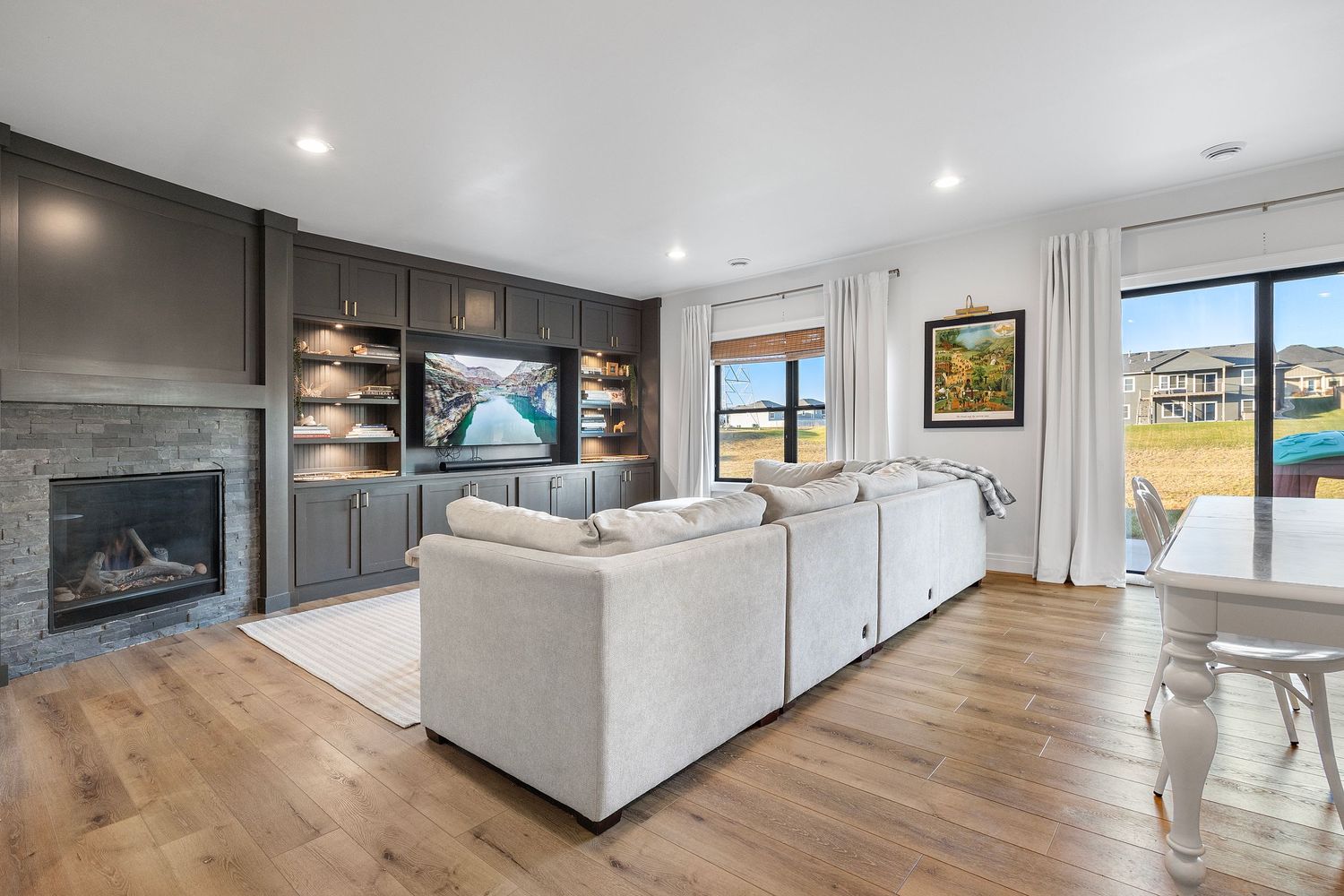 Modern living room with stone fireplace, grey built-ins, hardwood floors, and sliding doors leading to outdoor patio area.