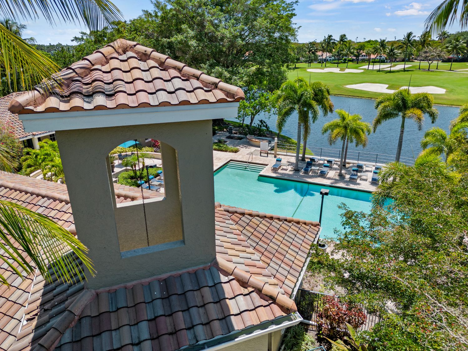 Aerial view of a luxury Florida swimming pool with clay tile roofs and palm trees overlooking a golf course lake.