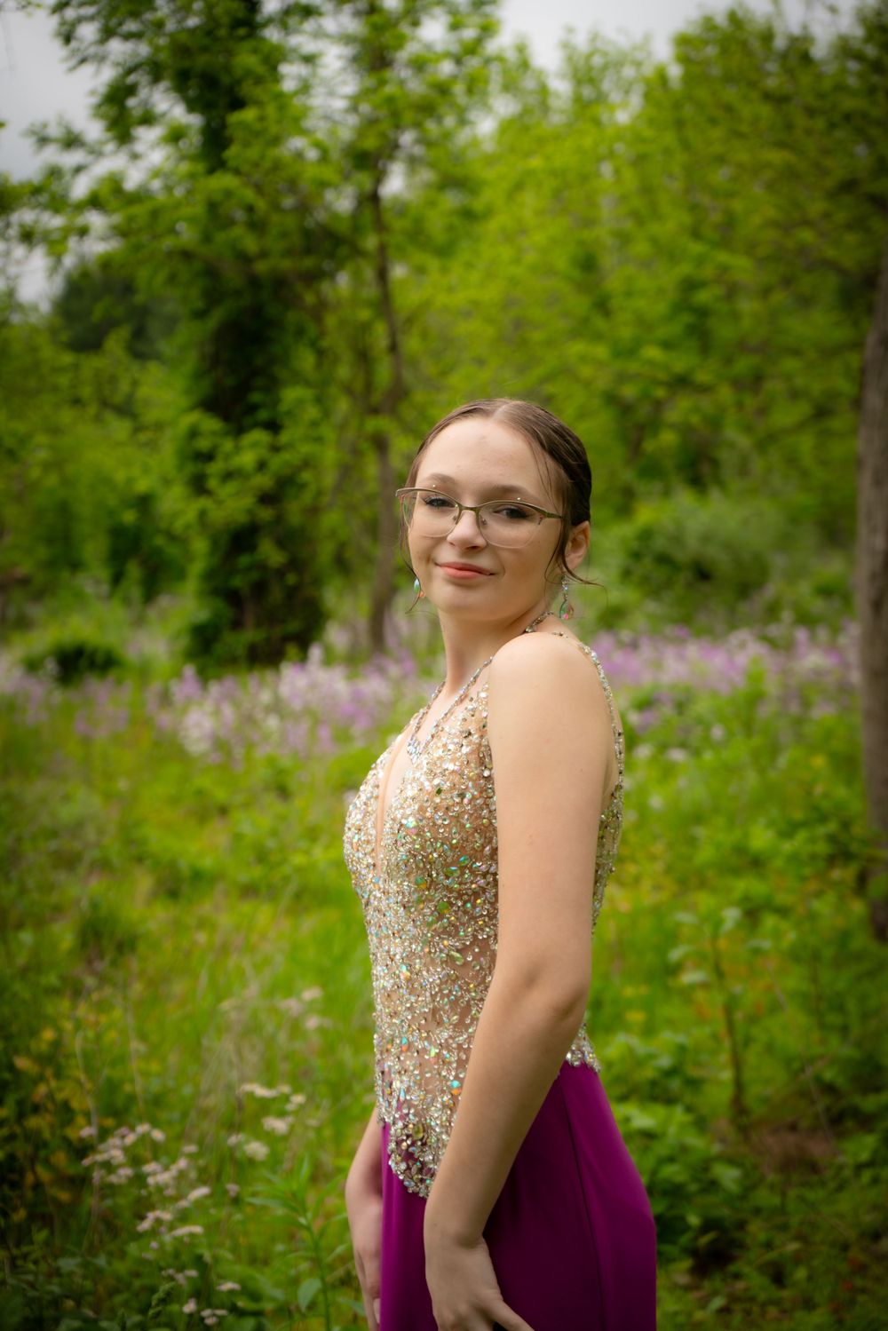 Person in sparkly formal dress poses in meadow with purple wildflowers.