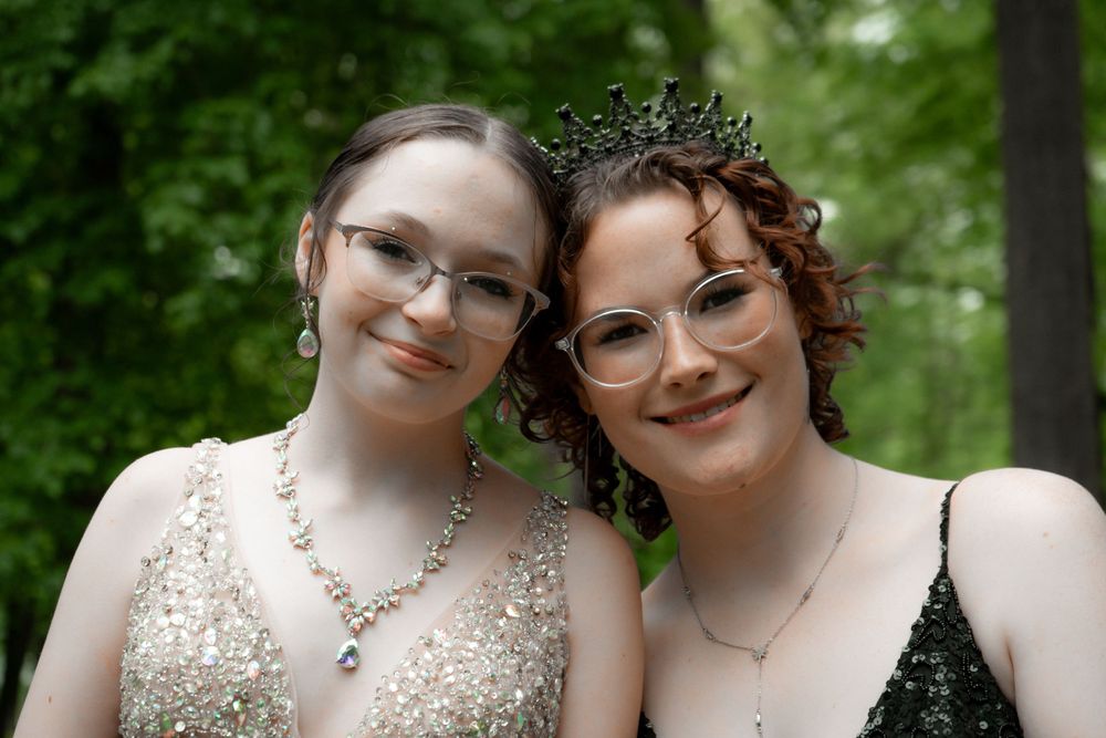 Friends pose in formal attire against green foliage background.