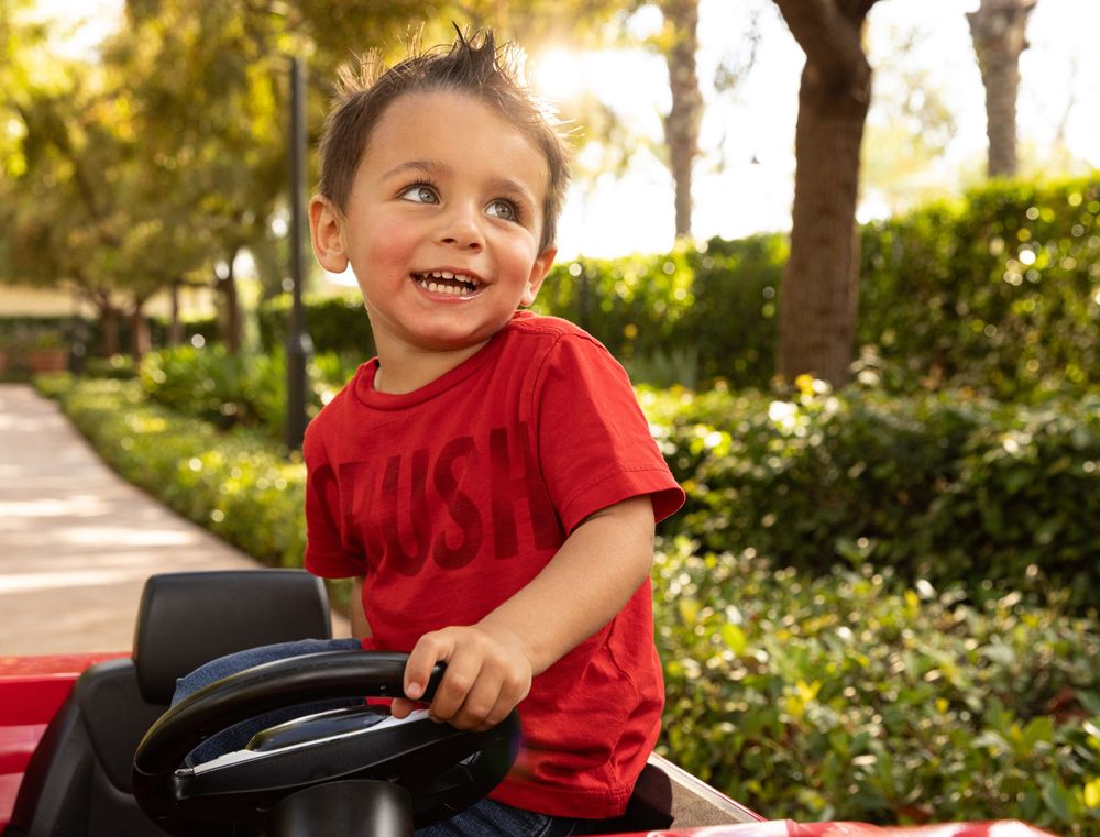 Lifestyle photograph of a smiling child with greenery and sunset glow in the background.