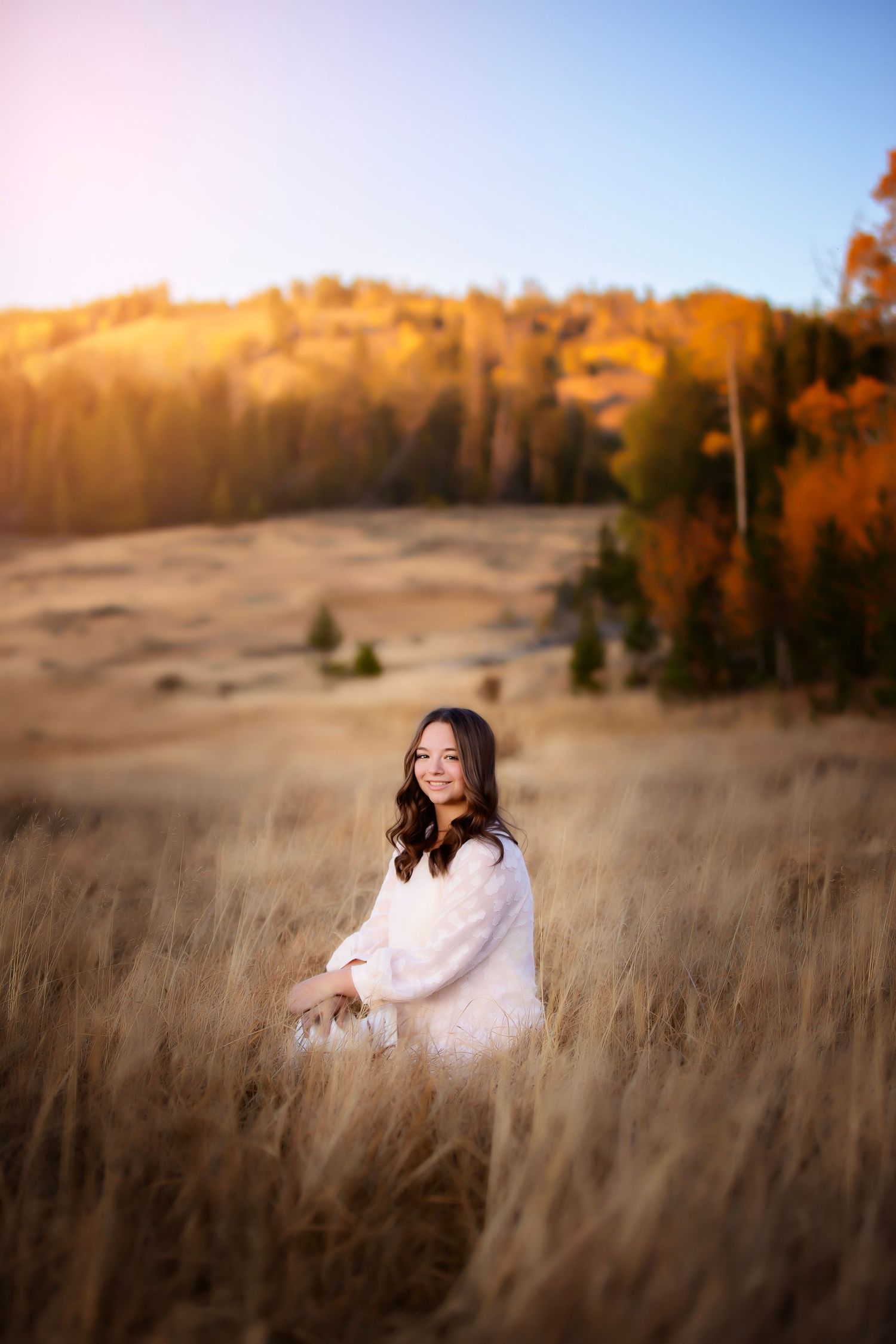 A golden hour portrait in a field with autumn mountains in the background.