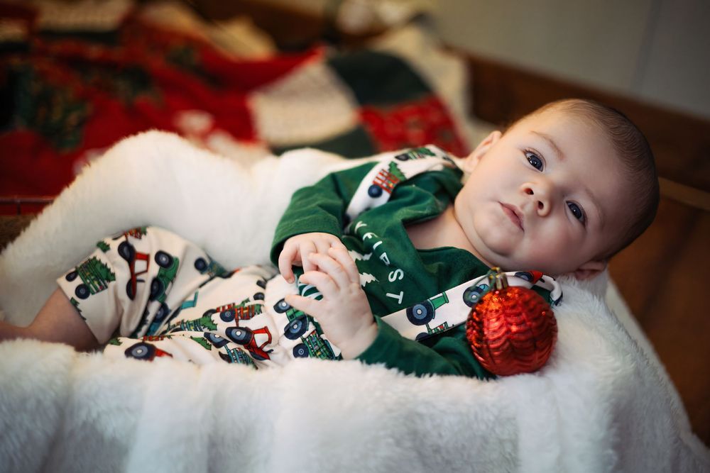 A series of photos showing a baby lying down in a festive green outfit surrounded by Christmas decorations and lights.
