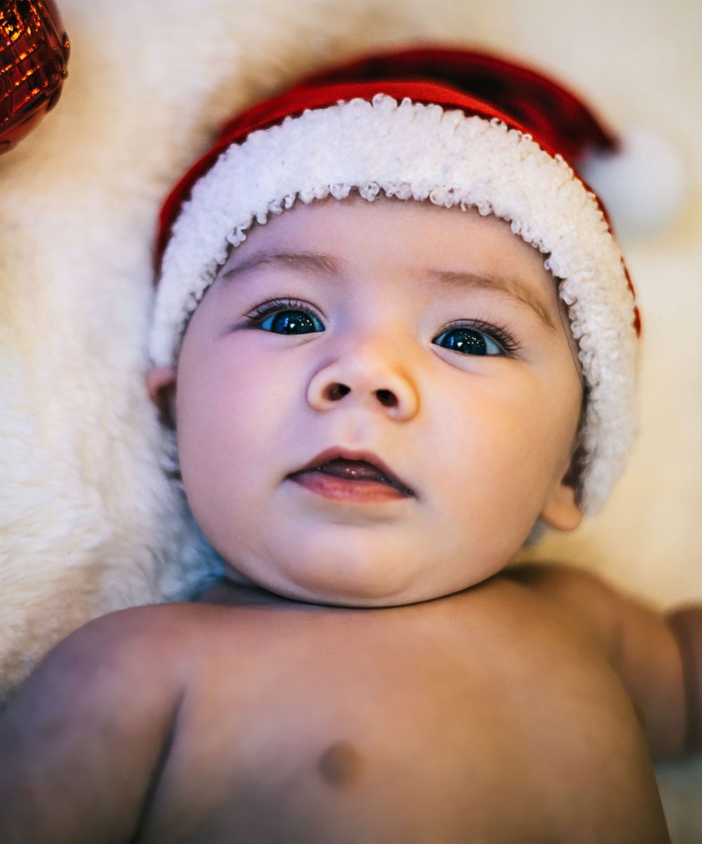 Artistic close-up portrait of baby in white Santa hat against soft blurred background.