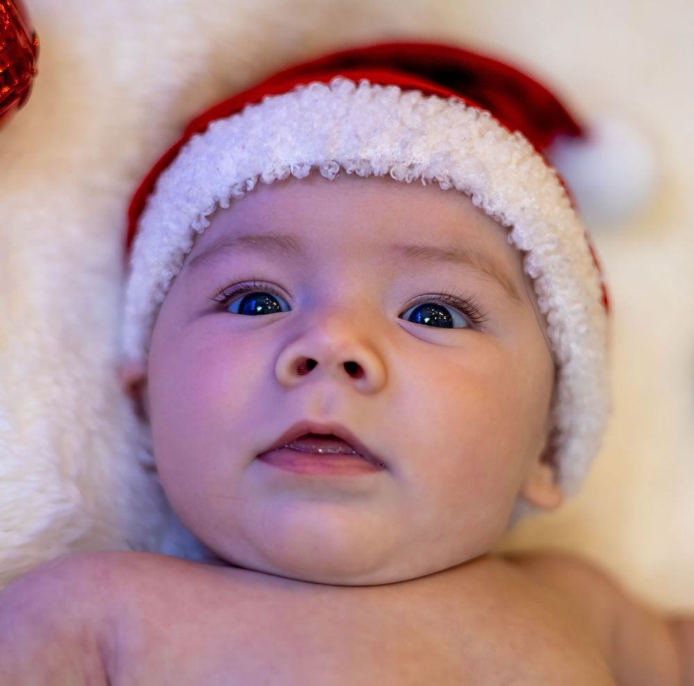 Baby wearing white Santa hat and white outfit smiling and making playful expressions in series of close-up photos.