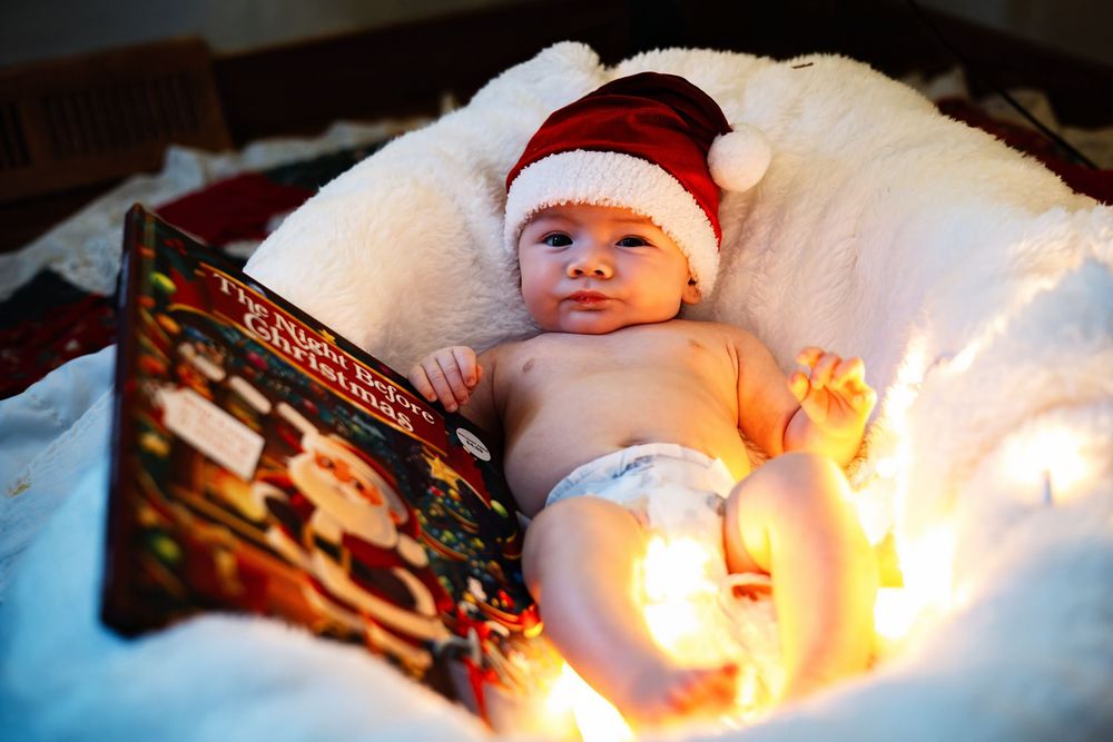 A close-up black and white photo of a baby wearing a white Santa hat.