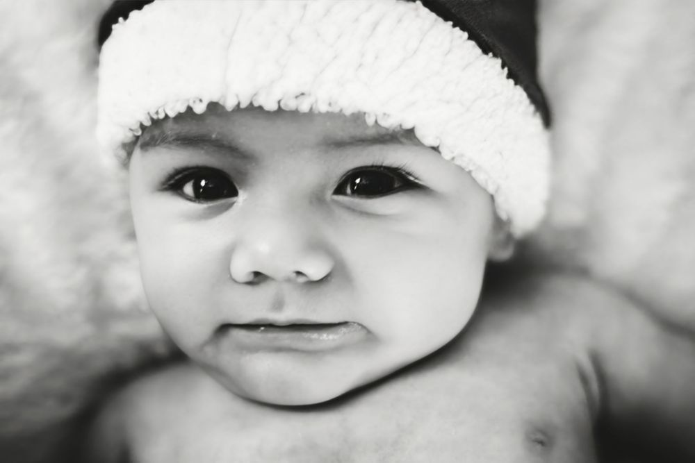 A series of black and white portraits showing a baby in a Santa hat with different expressions.