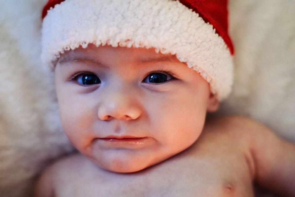 A baby wearing a red and white Santa hat smiles at the camera.