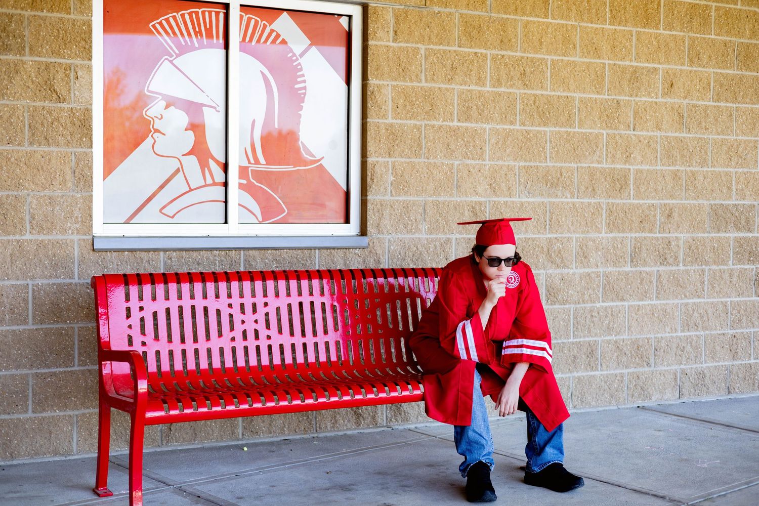 A red metal bench sits against a brick wall with a decorative framed artwork above it.