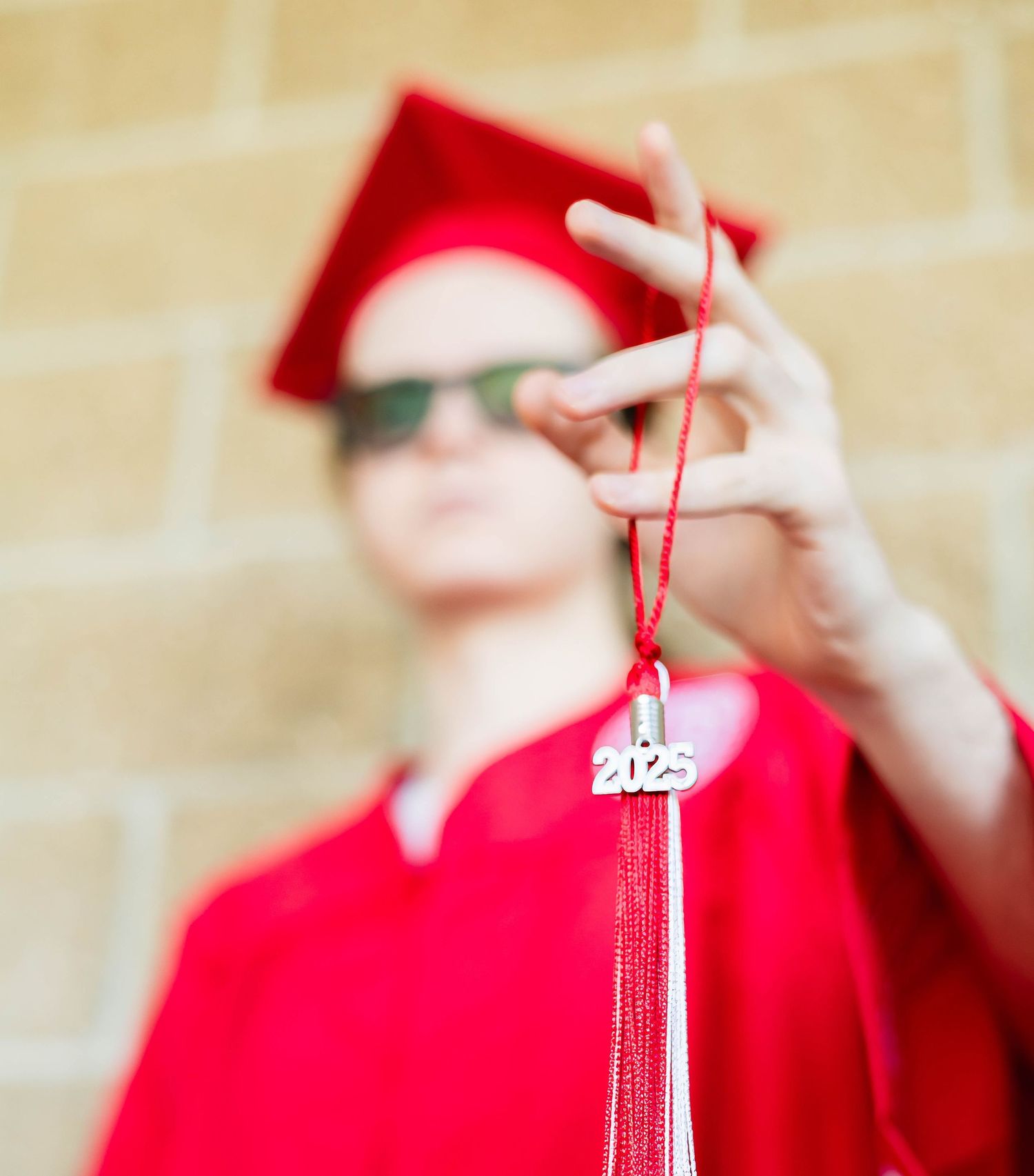 Graduate in red cap and gown holds up a class tassel against a blurred background.