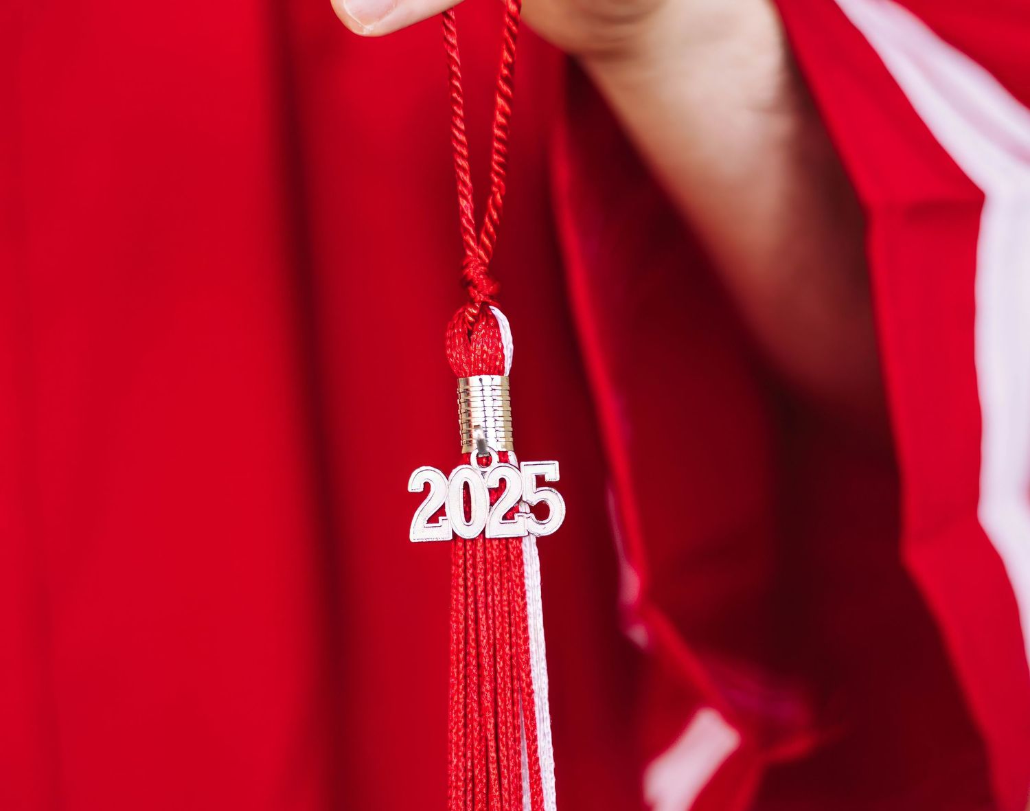A red graduation tassel with the year 2025 charm hanging against a bright red background.