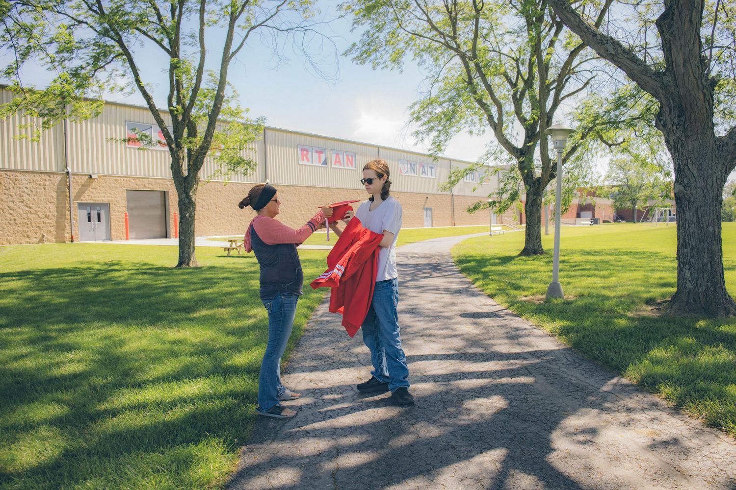 Three people in graduation attire stand together on a sunny path with trees in the background.
