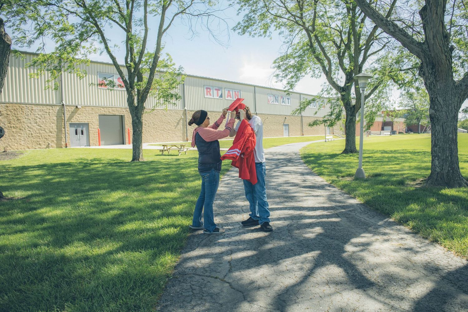 Two figures sharing a celebratory moment outdoors on a sunny spring day near campus buildings.
