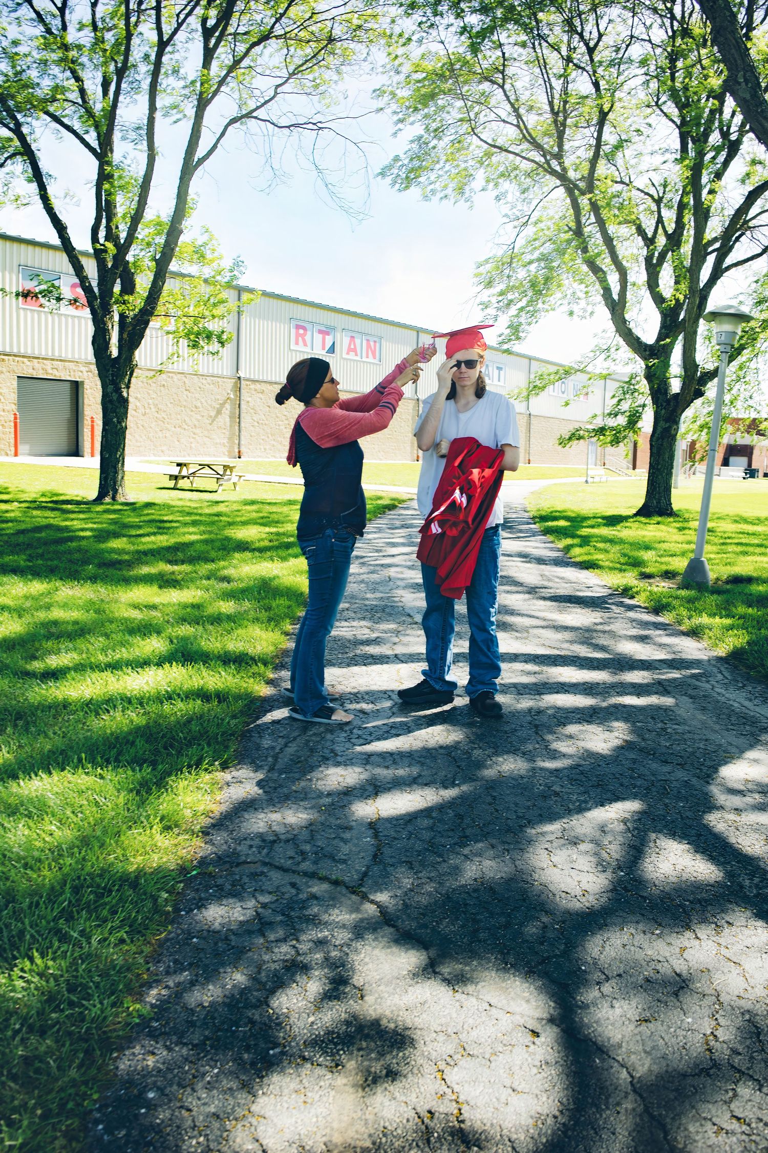 A graduation celebration moment captured on a tree-lined pathway with dappled sunlight.