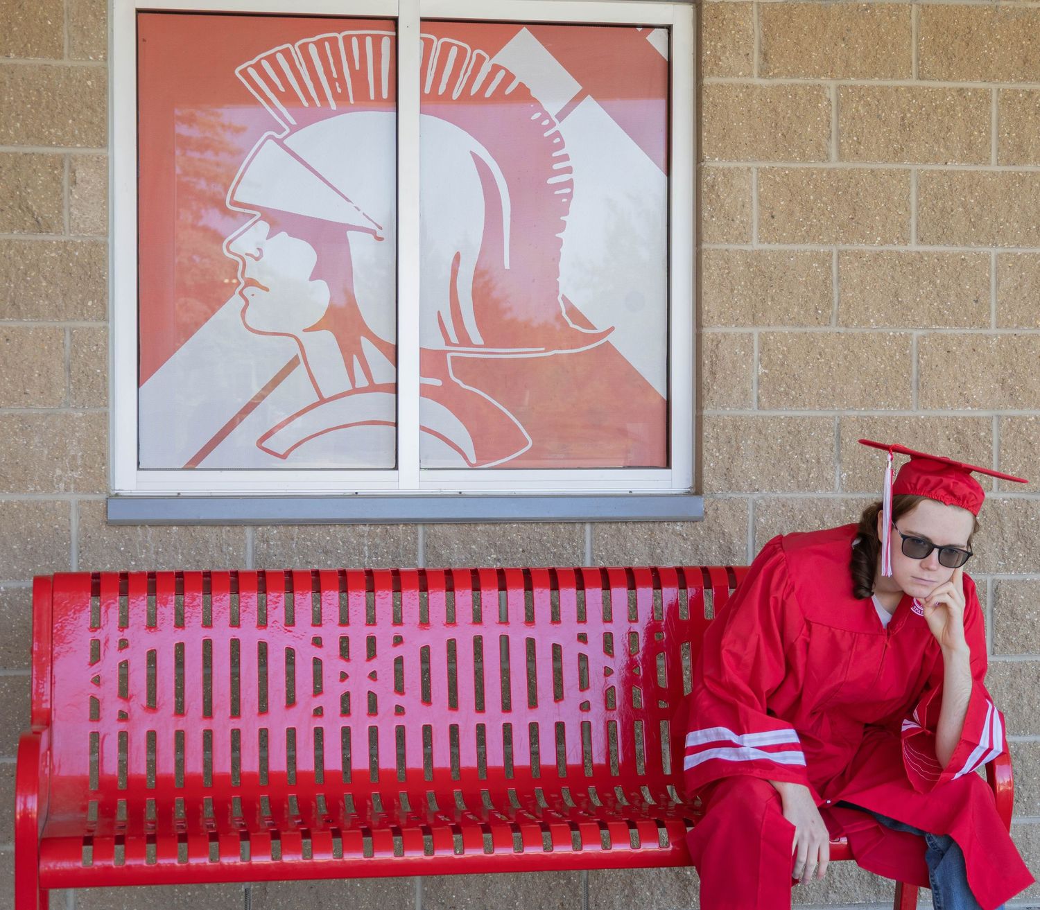 Red bench outside school building with Spartan warrior logo displayed in window.