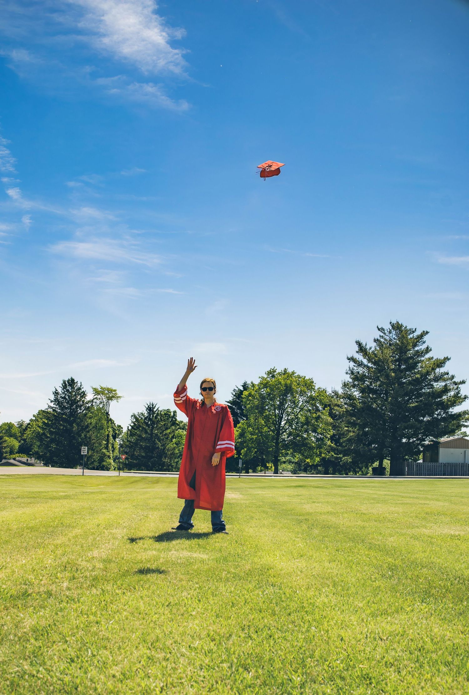 Graduate in red gown tosses cap into bright blue sky on sunny graduation day.