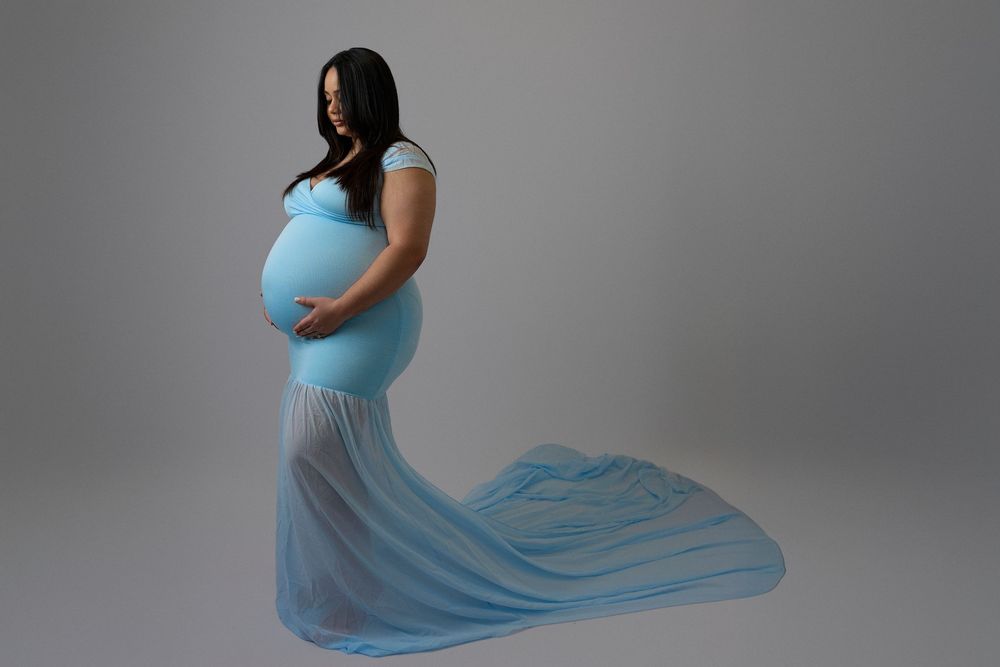 A flowing light blue maternity gown billows elegantly in a series of artistic pregnancy photos against a grey backdrop.
