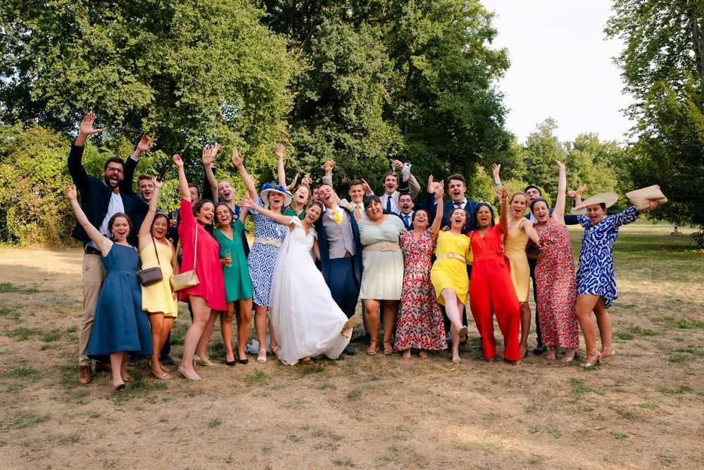 A large wedding party poses together outdoors in colorful dresses and attire during a summer celebration.