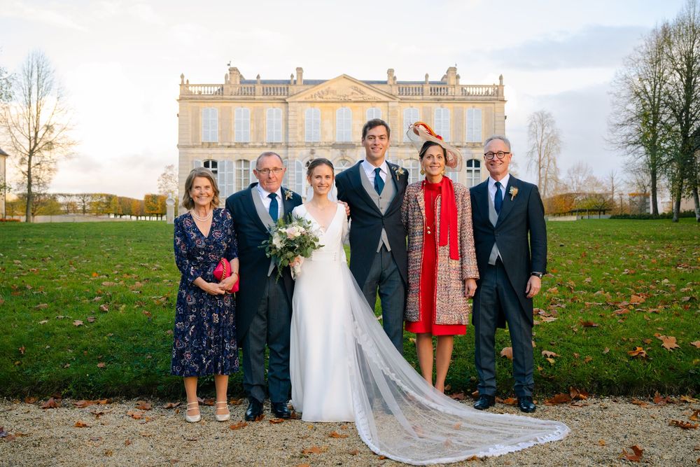 Wedding party poses together on an autumn day with fallen leaves on the grass and a grand building in the background.