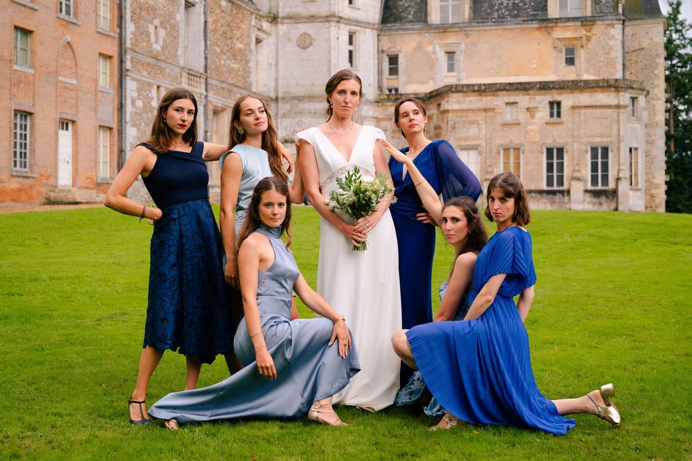 Wedding party in blue dresses poses playfully on castle grounds during outdoor celebration.