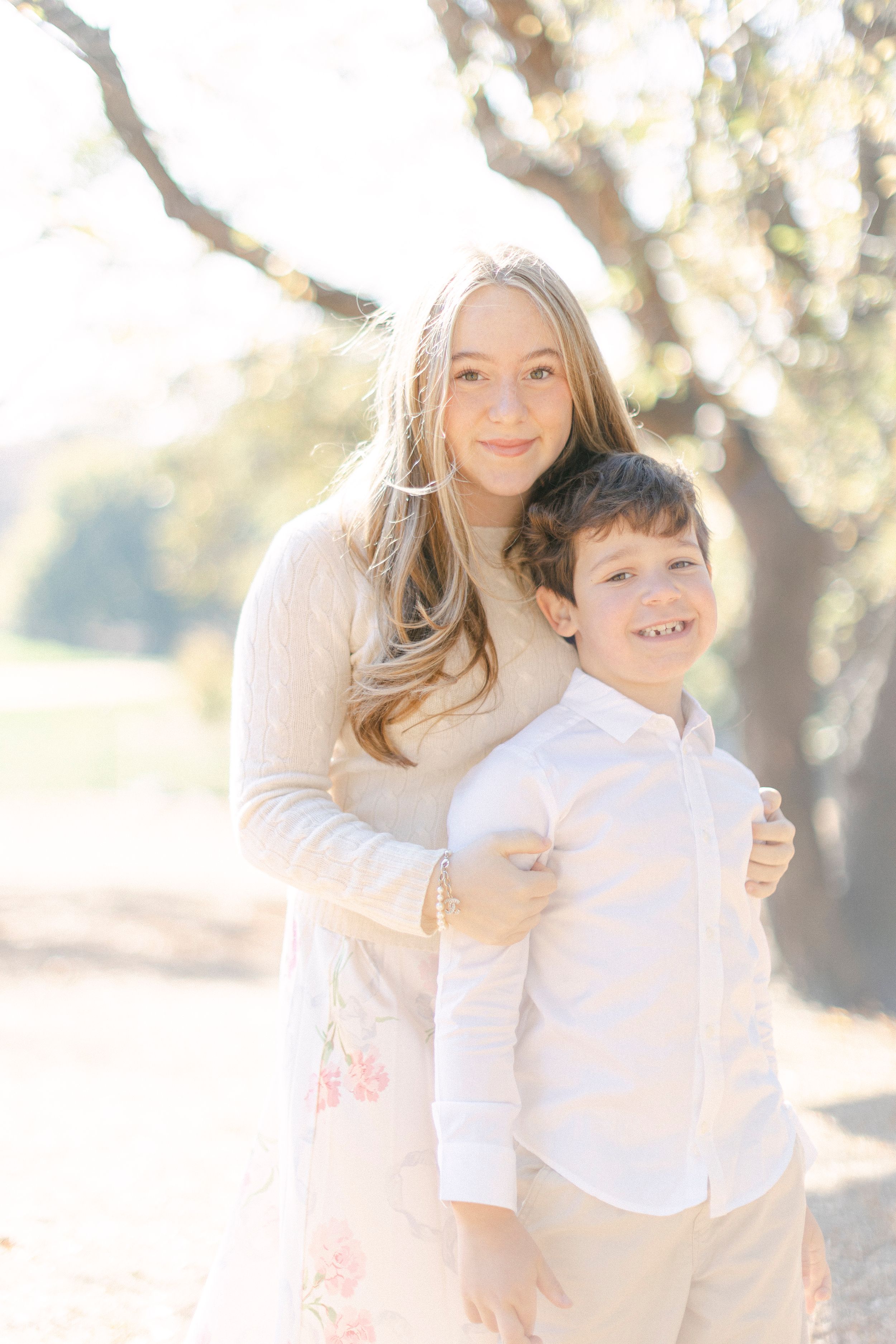 Two people share a warm embrace while posing for a portrait in dappled sunlight.