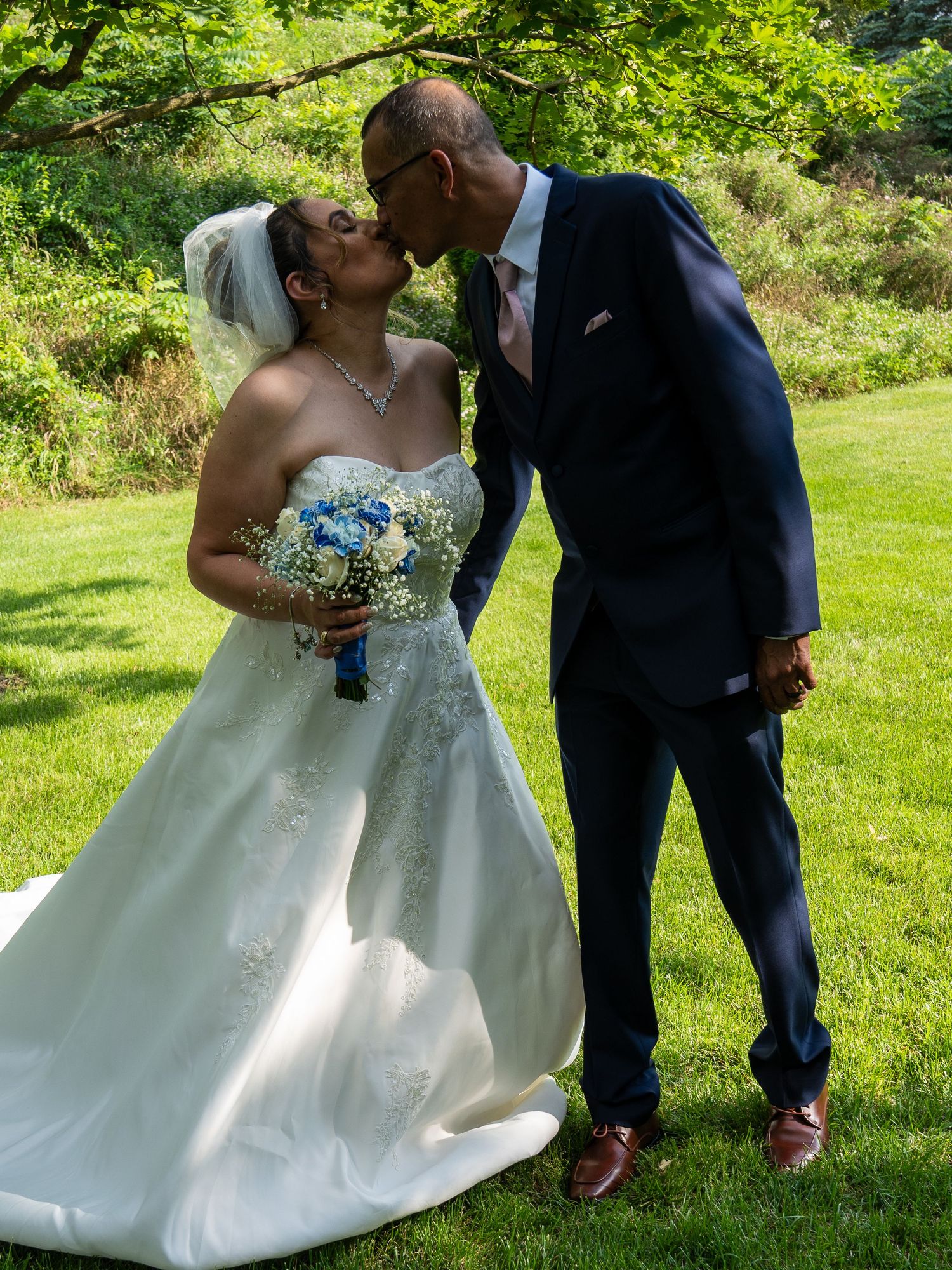 Romantic wedding couple sharing a kiss in a garden setting with blue and white bouquet.