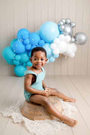 Portrait of child in turquoise outfit with blue and silver balloon arch backdrop.