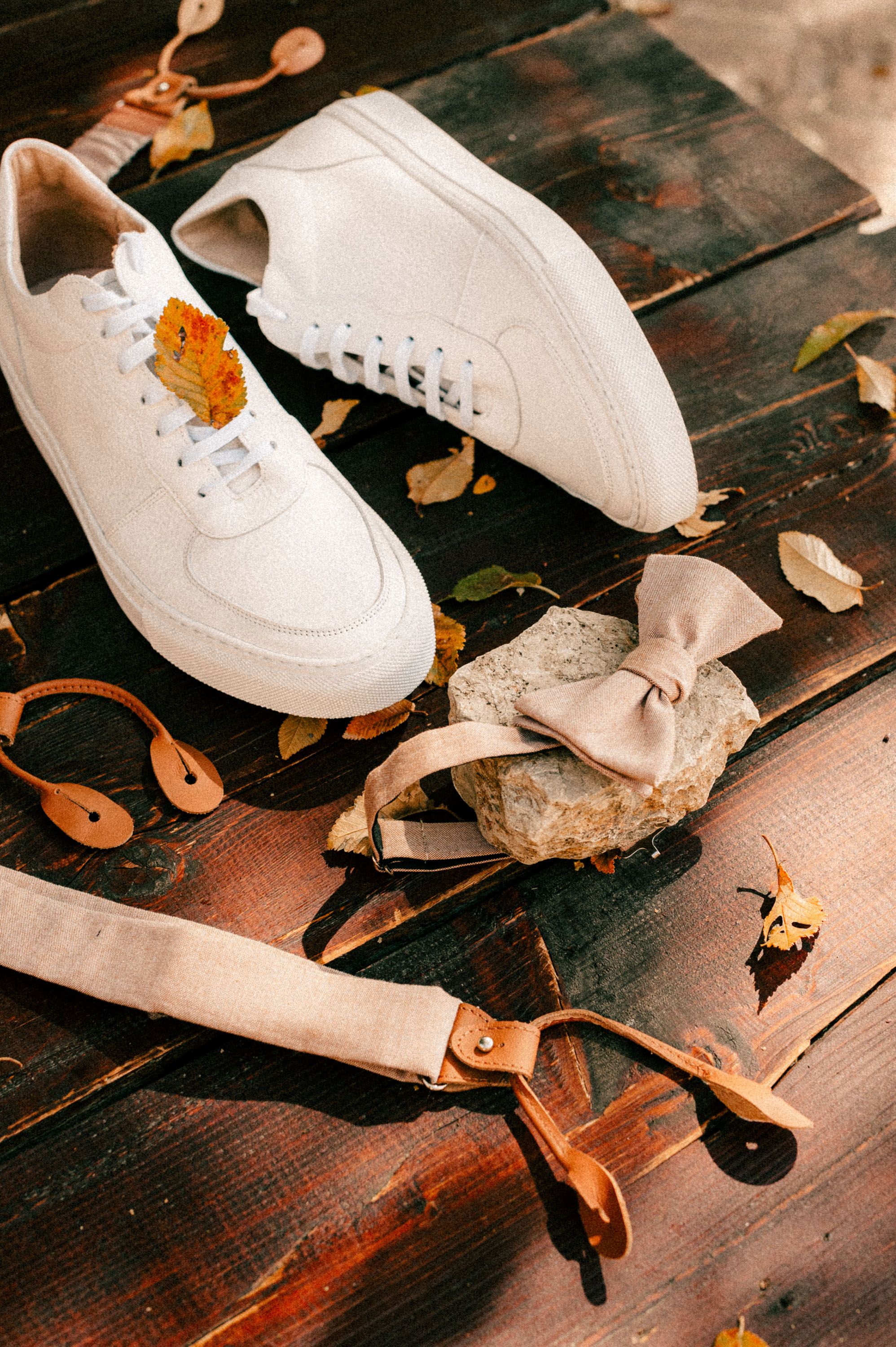 White sneakers and wedding accessories arranged on a dark wooden surface with autumn leaves.