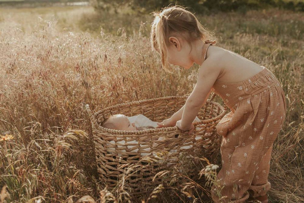 baby in a basket and little girl in an open field at golden hour with a spokane family photographer
