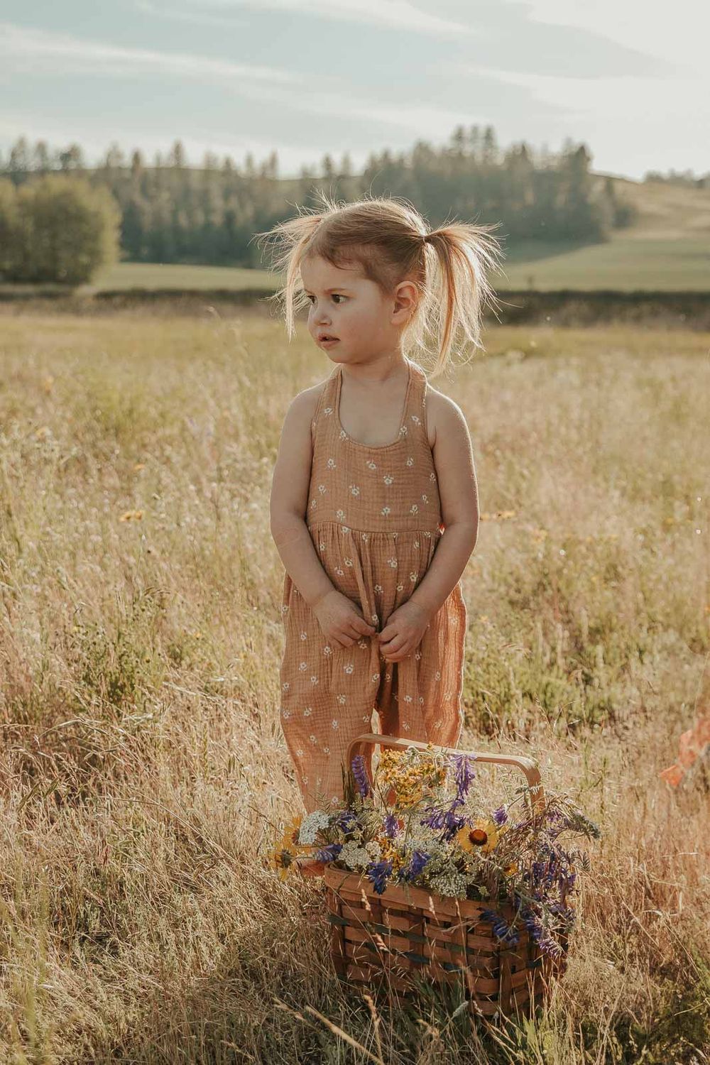 little girl in a brown romper in an open field at golden hour with a spokane family photographer