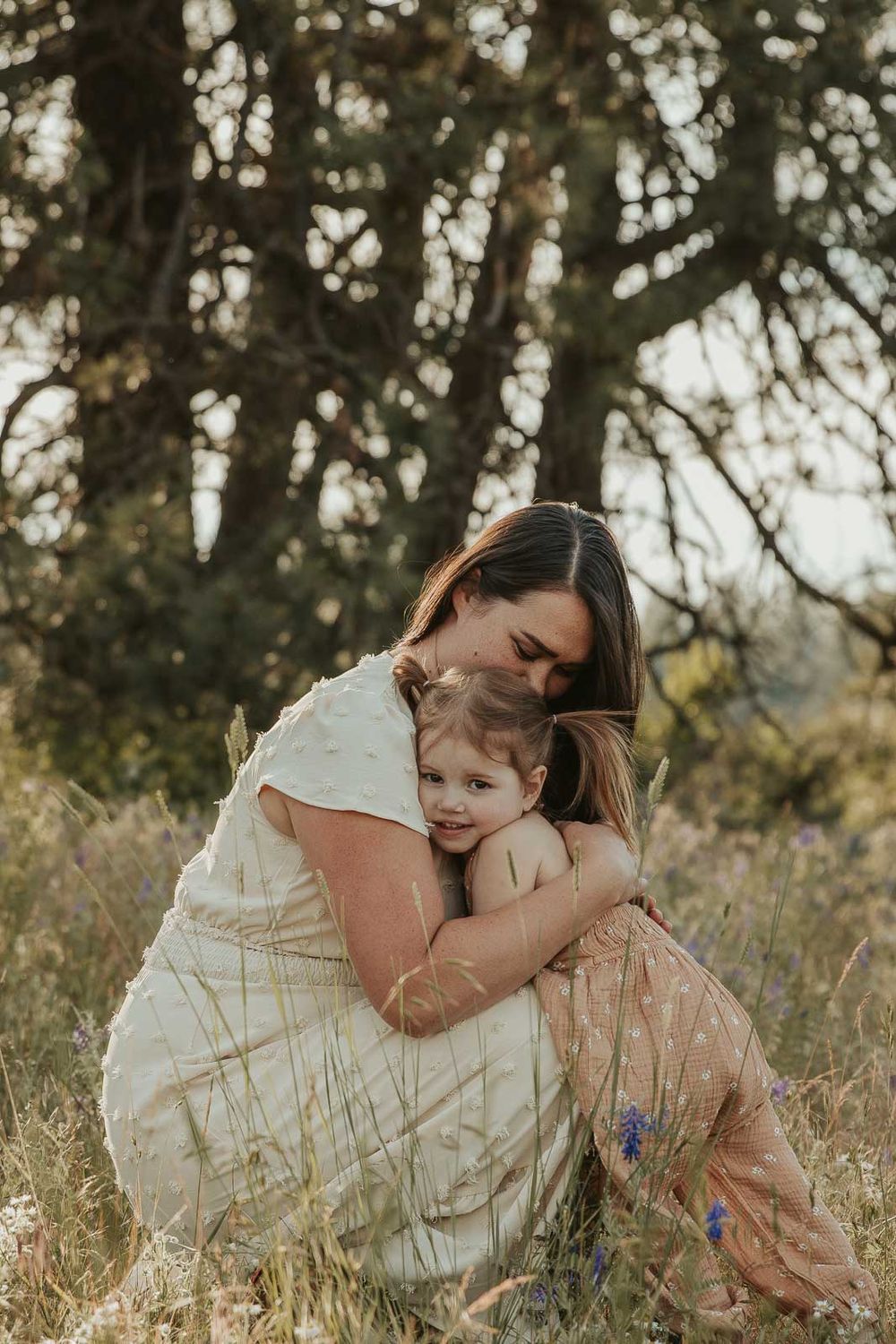 mother and daughter in earth tone dresses hugging in a flower field at golden hour with a spokane family photographer