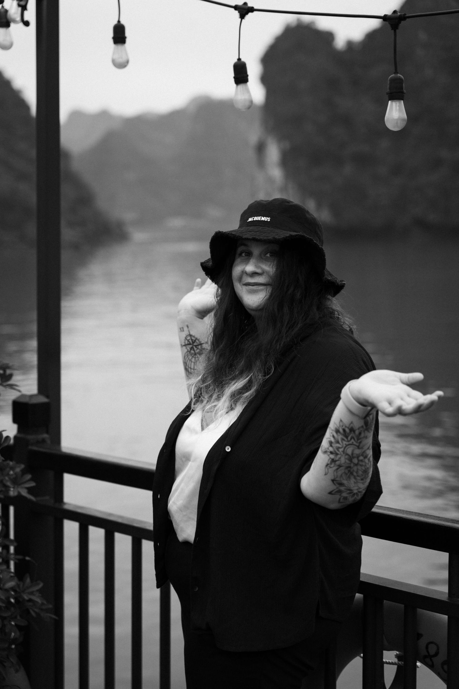 A casual portrait on a deck with hanging string lights and a lake view in black and white.