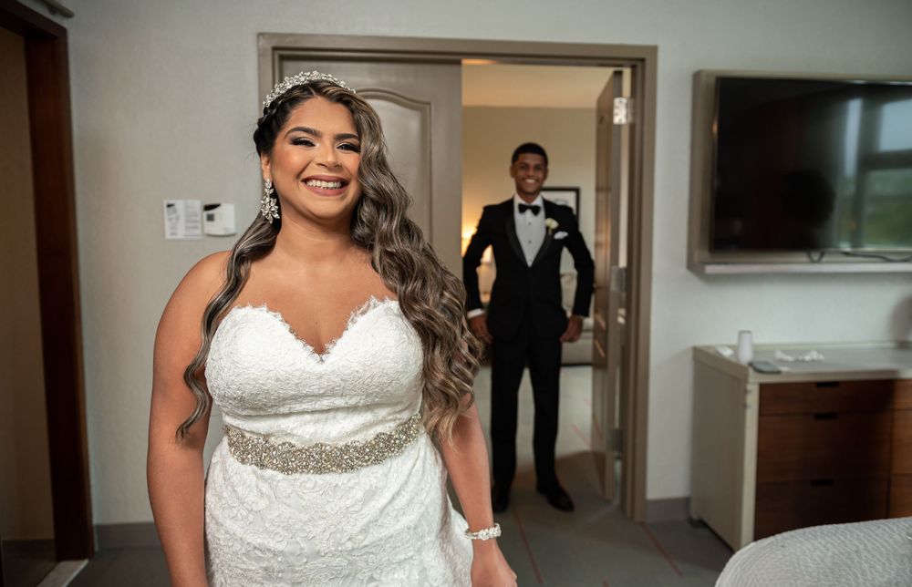 Bride in lace wedding dress smiles radiantly during first look moment.