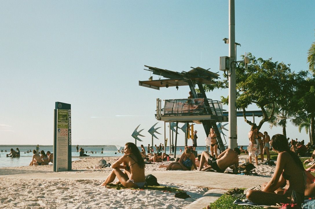 Beachgoers relax under palm trees and lifeguard tower on sunny tropical shoreline.