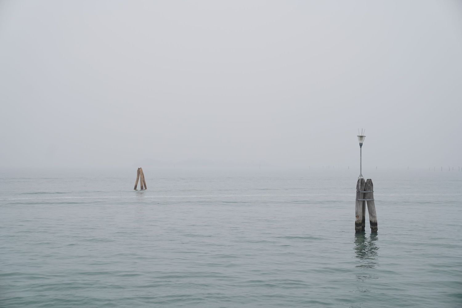 Minimalist seascape with wooden posts emerging from foggy waters.