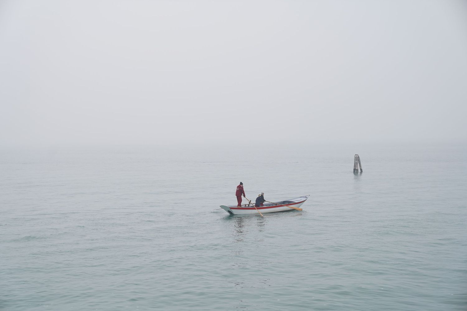 Small boat with figures floating in misty ocean waters with a windsurfer in the distance.