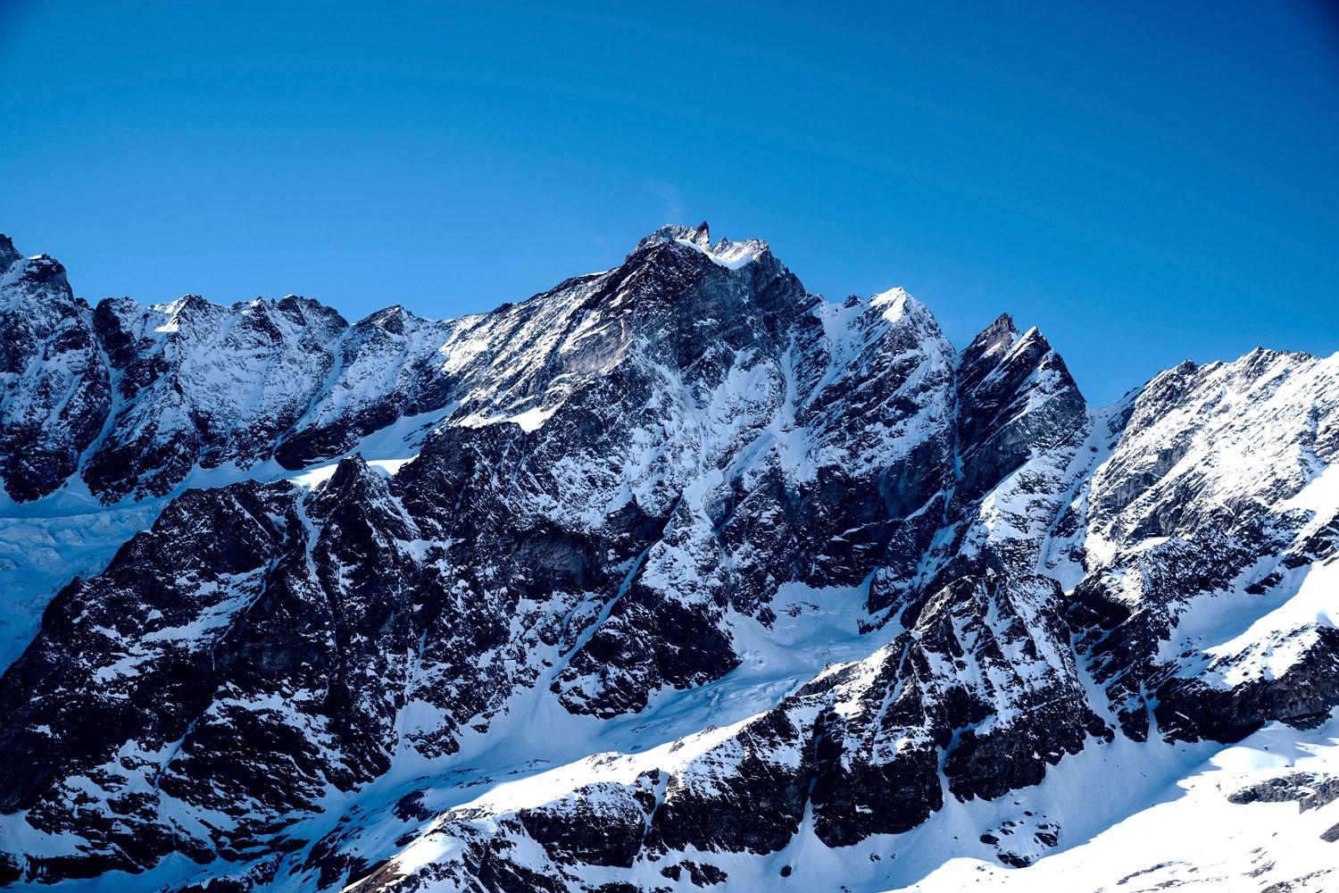 Snow-capped rocky mountain peaks against deep blue sky in dramatic alpine landscape.